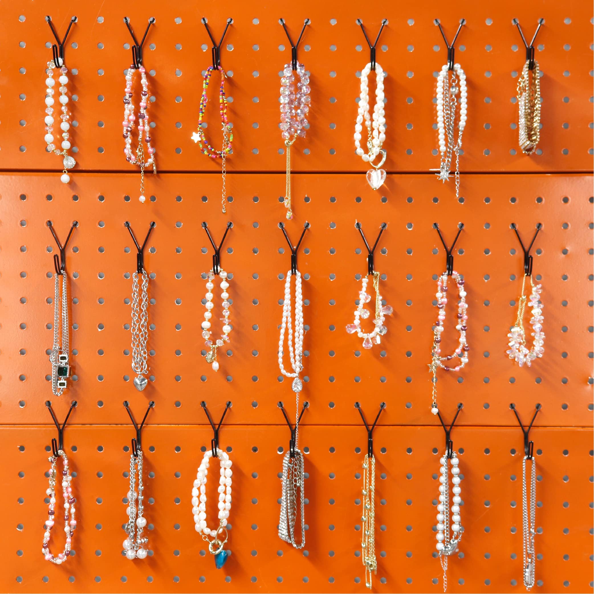 This image showcases an expertly organized jewelry display using a pegboard system with Huhole-style hooks. The pegboard, in a vibrant orange color, serves as the backdrop for an array of necklaces, bracelets, and other jewelry pieces. 