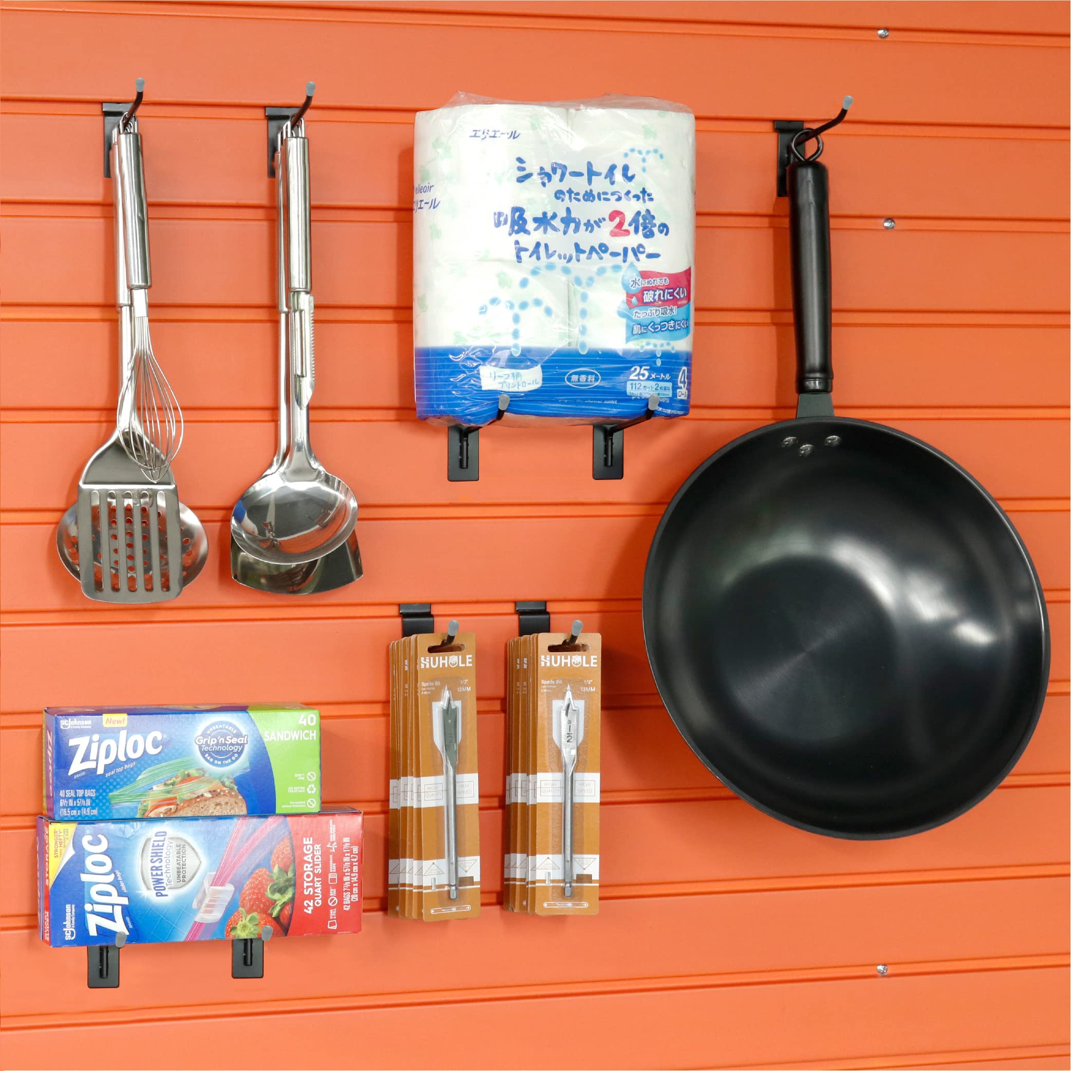 This image shows an organized storage display using a slatwall system in what appears to be a garage or utility space. The slatwall is used to neatly arrange a variety of kitchen-related items, including cooking utensils, a large pan, and cleaning supplies like Zipoc bags.